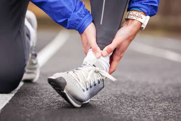 A person holding a painful ankle after an injury, the kind of ankle pain and sprains Dr. Hubert Lee treats at CarePlus in Bellevue