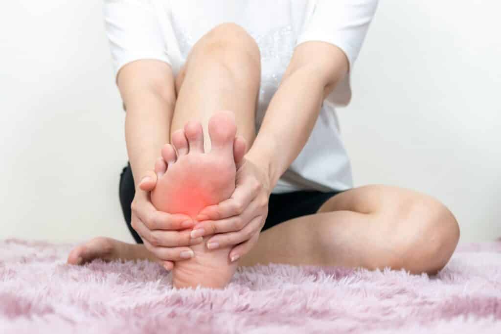A woman touching her right foot showing nerve pain, indicating neuropathy treatment Dr. Hubert Lee provides