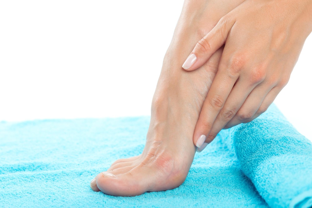 woman's hand touching her raised foot on a blue towel