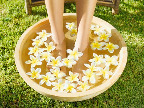 Feet soaked in a basin with water covered in flower pedals, on green grass